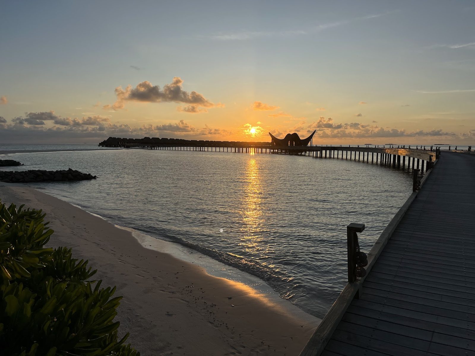 Sunset over a curved jetty and overwater villas, Maldives